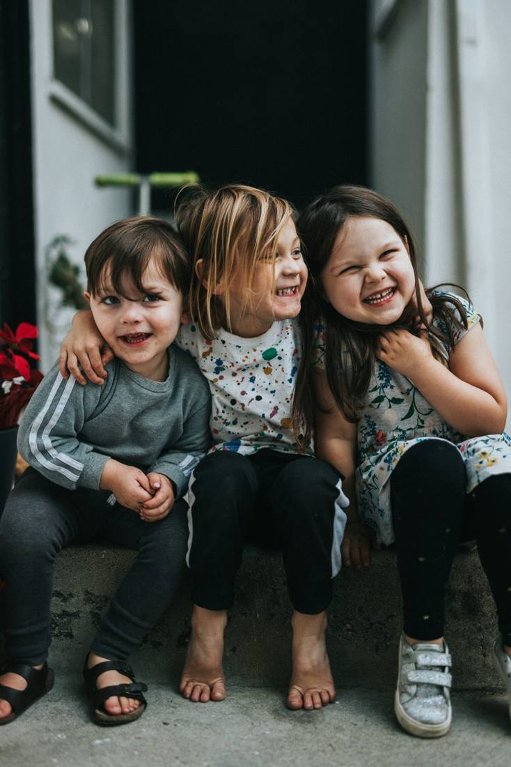 Three kids laughing and hugging on a front step
