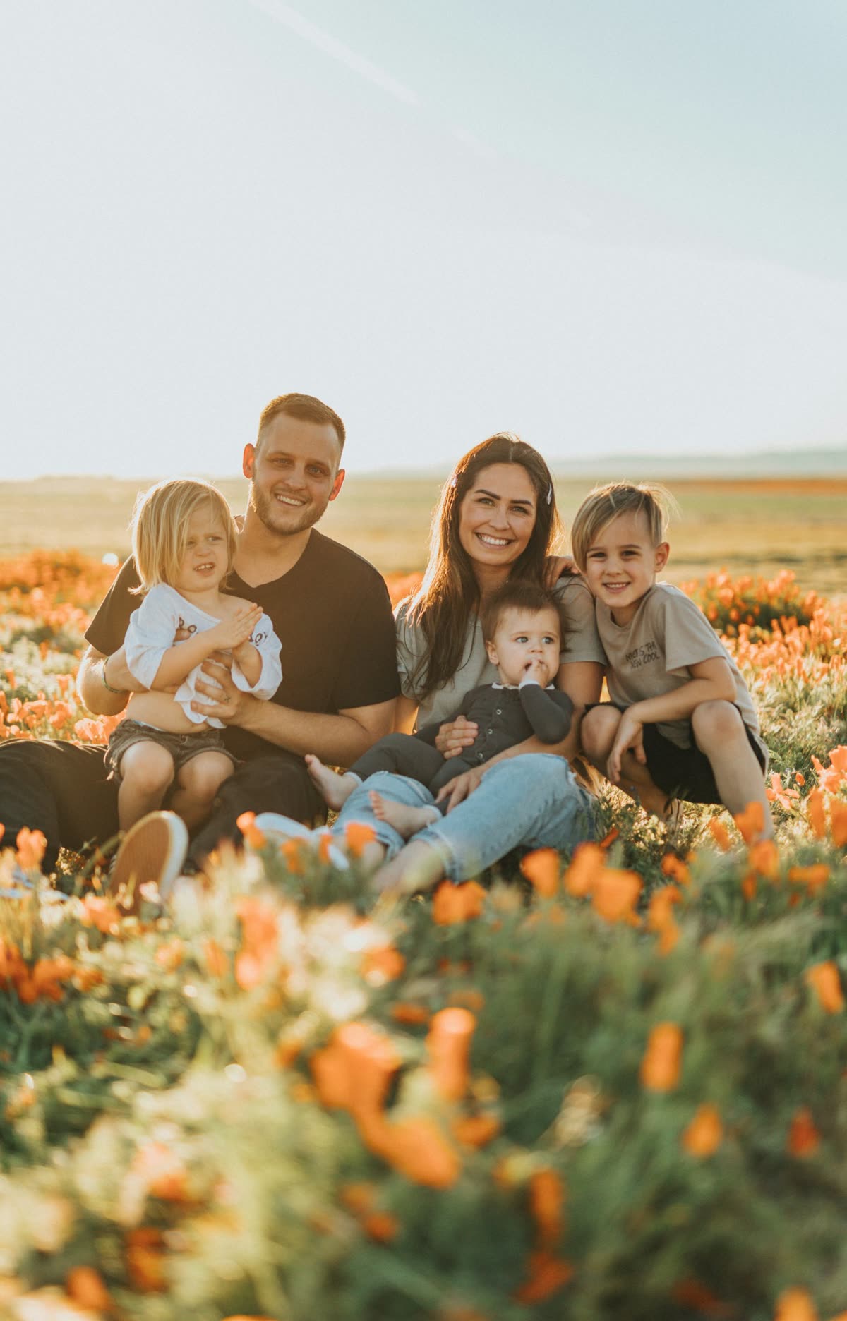 A smiling family of five sitting in a field of orange poppies