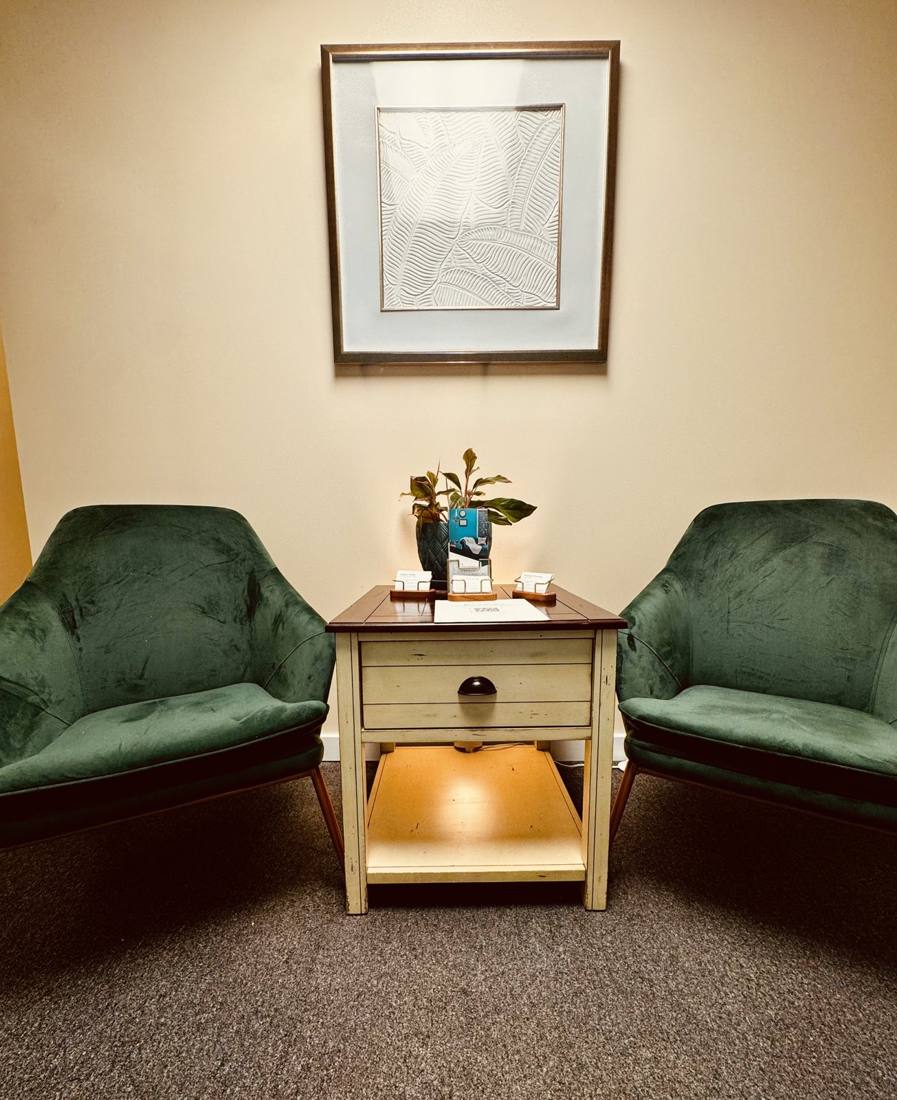 Two green velvet chairs and a side table with a plant in the waiting area